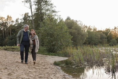 Man and woman walking together on sand by lake