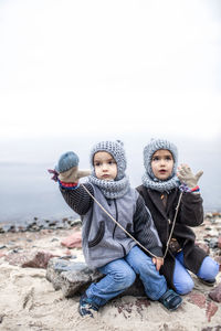 Cute cheerful sibling sitting by lake during winter