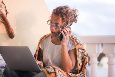 Woman using mobile phone and laptop while sitting at home