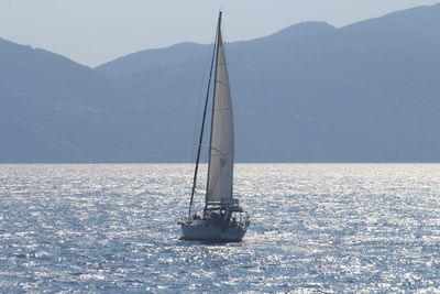 Sailboat sailing on sea against mountains