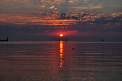 Sun reflecting in sea against cloudy sky at sunset