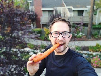 Portrait of man eating carrot at backyard