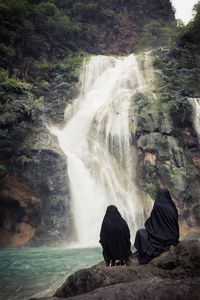 Women sitting on rocks against waterfall