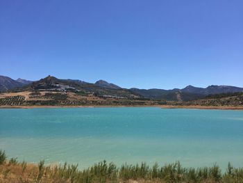 Scenic view of sea and mountains against clear blue sky