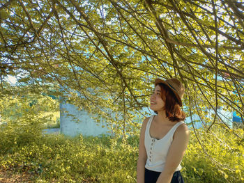 Young woman looking away while standing against plants