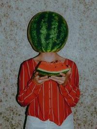 Midsection of man holding strawberry while standing against wall