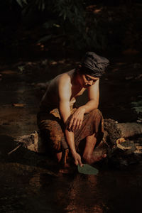 Side view of man sitting on rock