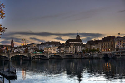 Bridge over river by buildings against sky at dusk