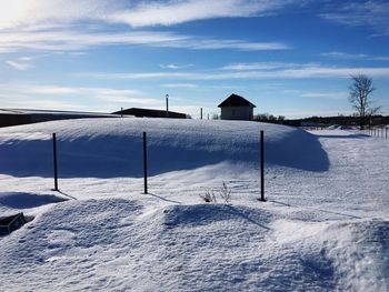 Snow covered field by houses against sky