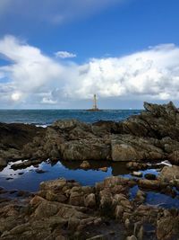 View of lighthouse in sea with rock formation beach against sky 