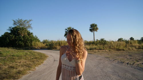 Young woman standing on road against clear blue sky during sunny day