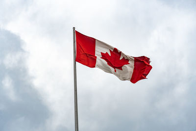 Low angle view of canadian flag waving on pole against sky