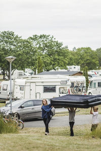 Children carrying inflatable mattress together while walking against trailers at camping site