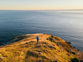 Rear view of man looking at sea while standing at cliff