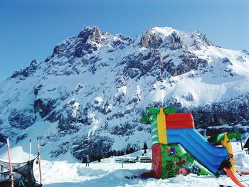 Outdoor play equipment on snow covered land against mountain