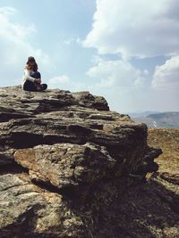 High angle view of woman sitting on cliff by sea against sky