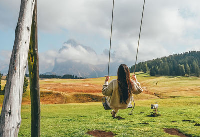 Rear view of woman on swing against mountains