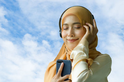 Portrait of smiling young woman using smart phone against sky