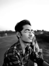 Portrait of young man wearing sunglasses standing at beach against clear sky