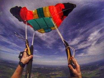 Cropped hands of man paragliding over landscape against sky