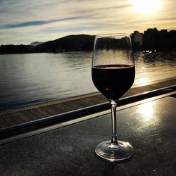 Close-up of wineglass against river during sunset