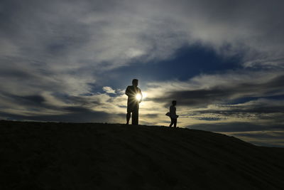 Silhouette couple standing on land against sky during sunset