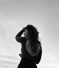 Side view of young woman standing against sky