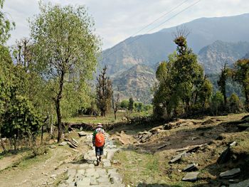 Rear view of hiker walking on footpath by mountain against sky