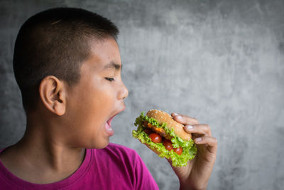 Close-up of boy eating burger against wall