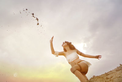 Woman throwing sand at beach against sky during sunset