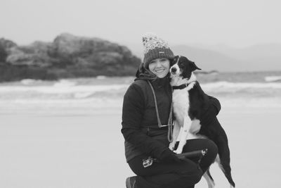 Portrait of smiling woman with dog at beach during winter