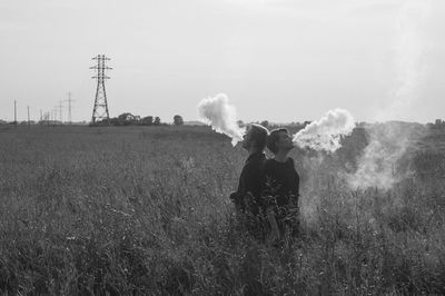 Friends exhaling smoke while standing on field