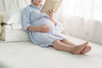 Midsection of woman sitting on bed at home