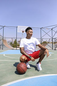 Young man crouching by basketball at sports court