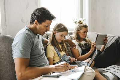 Father teaching daughter while mother sitting beside using digital tablet at home
