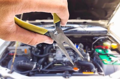 Cropped hand holding pliers against car engine