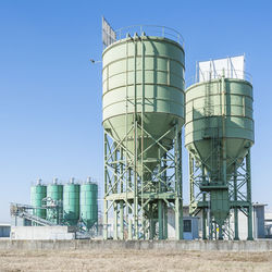 Low angle view of industrial silos against blue sky