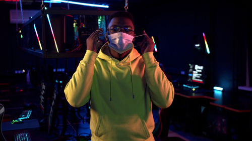 Portrait of young man wearing mask standing in internet cafe