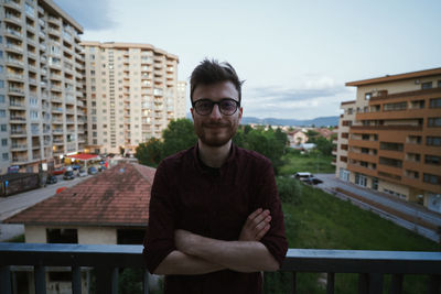 Portrait of young man standing against buildings in city