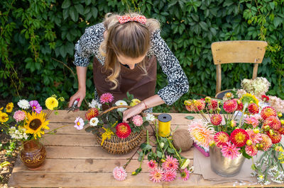 Cute florist girl collects a bouquet in a basket of autumn flowers