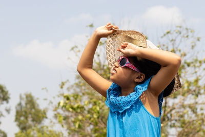 An indian girl wearing sunglasses and holding hat looking at the sun in summer