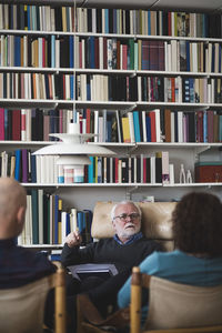 Senior therapist explaining couple while sitting against bookshelf