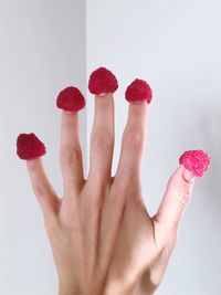 Close-up of hand with raspberries against wall