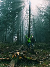 Friends enjoying while walking on field amidst trees in forest