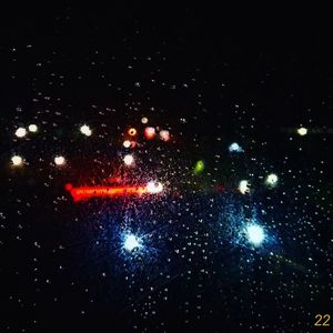 Raindrops on car windshield against sky at night