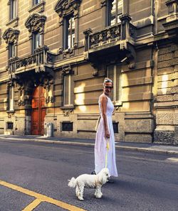 Beautiful woman with poodle standing on city street against old building