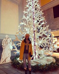 Full length of woman standing against illuminated christmas tree