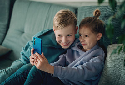 Portrait of happy friends using mobile phone while sitting on sofa at home