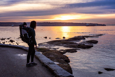 Rear view of woman walking on beach against sky during sunset