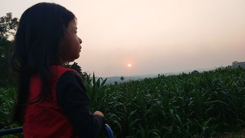 Side view of woman looking at field against sky during sunset
